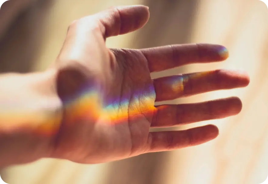 A person holding their hand in the sunlight so that a rainbow is visible on their palm.