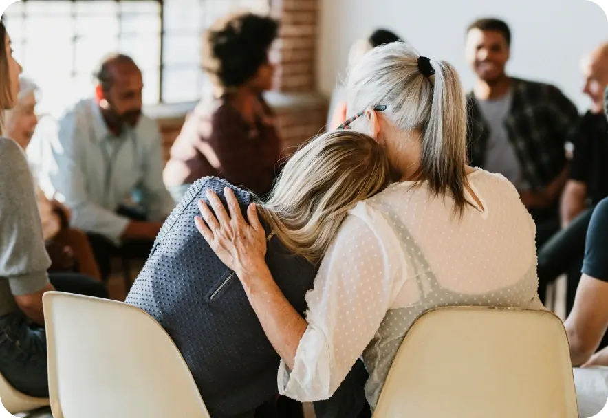 A woman leans her head on the shoulder of another person in group therapy session