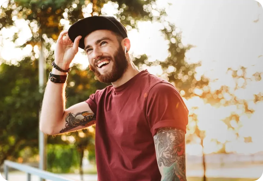 A man is smiling while holding right arm up to the ball cap on his head