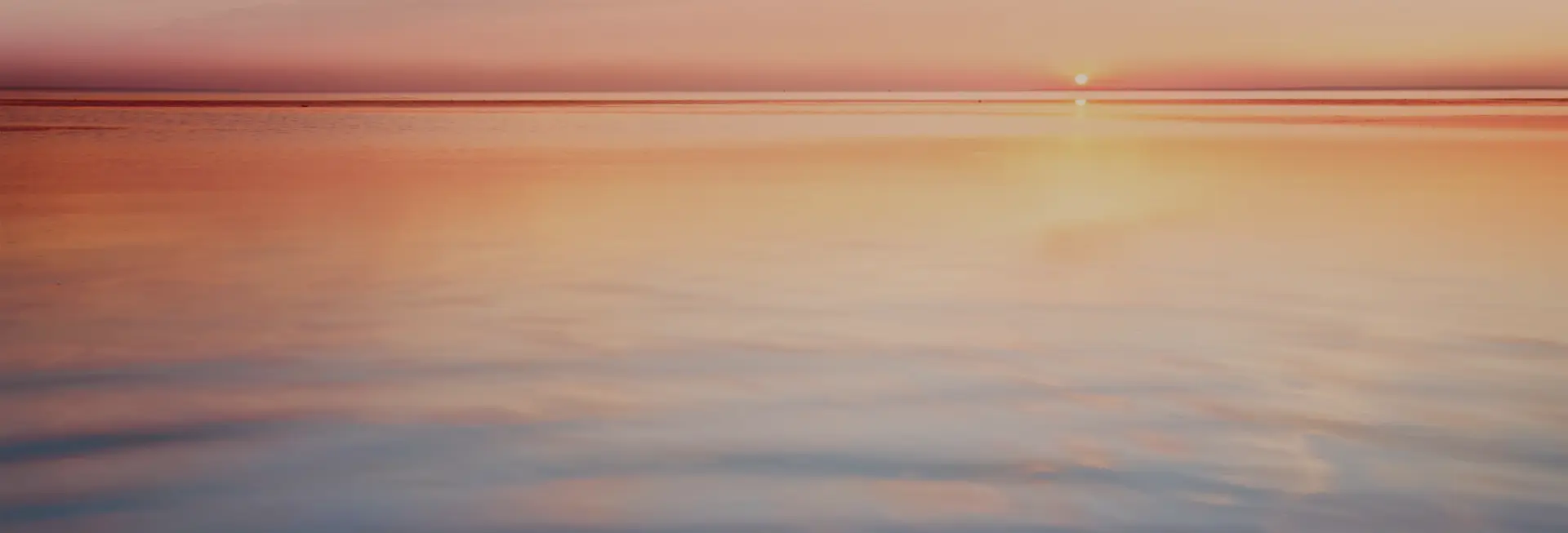 Still sea water at sunset with pink sky and orange and blue water