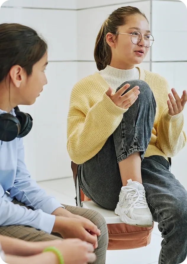 Person sitting on a chair with one foot up on the chair and the other on the ground.